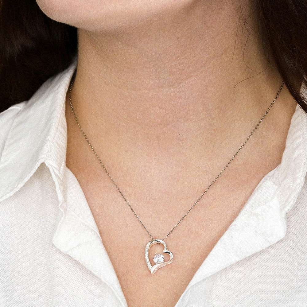 Silver heart-shaped necklace with a pendant on a person wearing a white shirt.