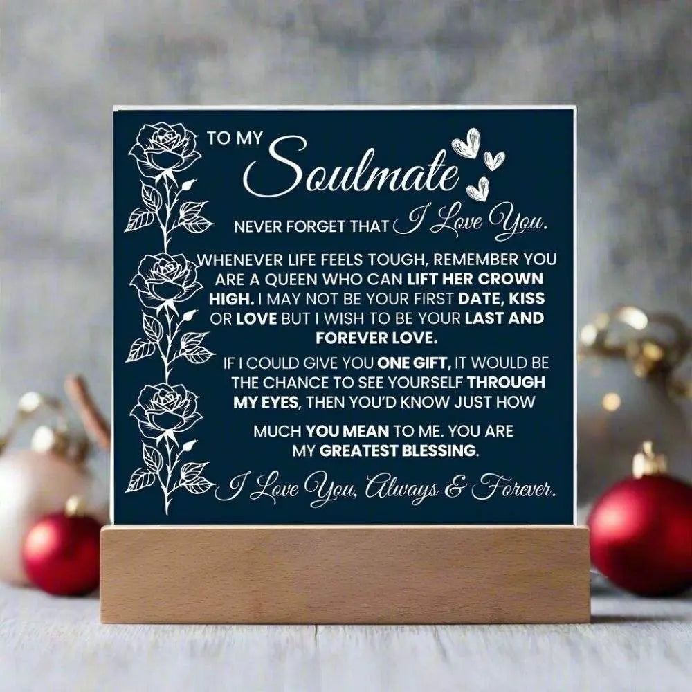 Navy blue sign with white text and floral designs on a wooden stand, set against a blurred decorative background.
