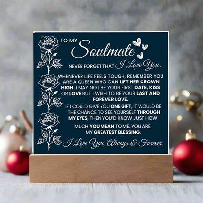 Navy blue sign with white text and floral designs on a wooden stand, set against a blurred decorative background.
