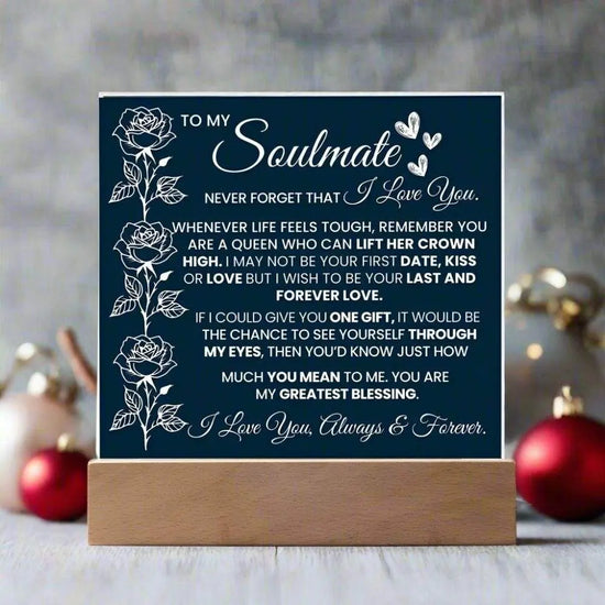 Navy blue sign with white text and floral designs on a wooden stand, set against a blurred decorative background.

