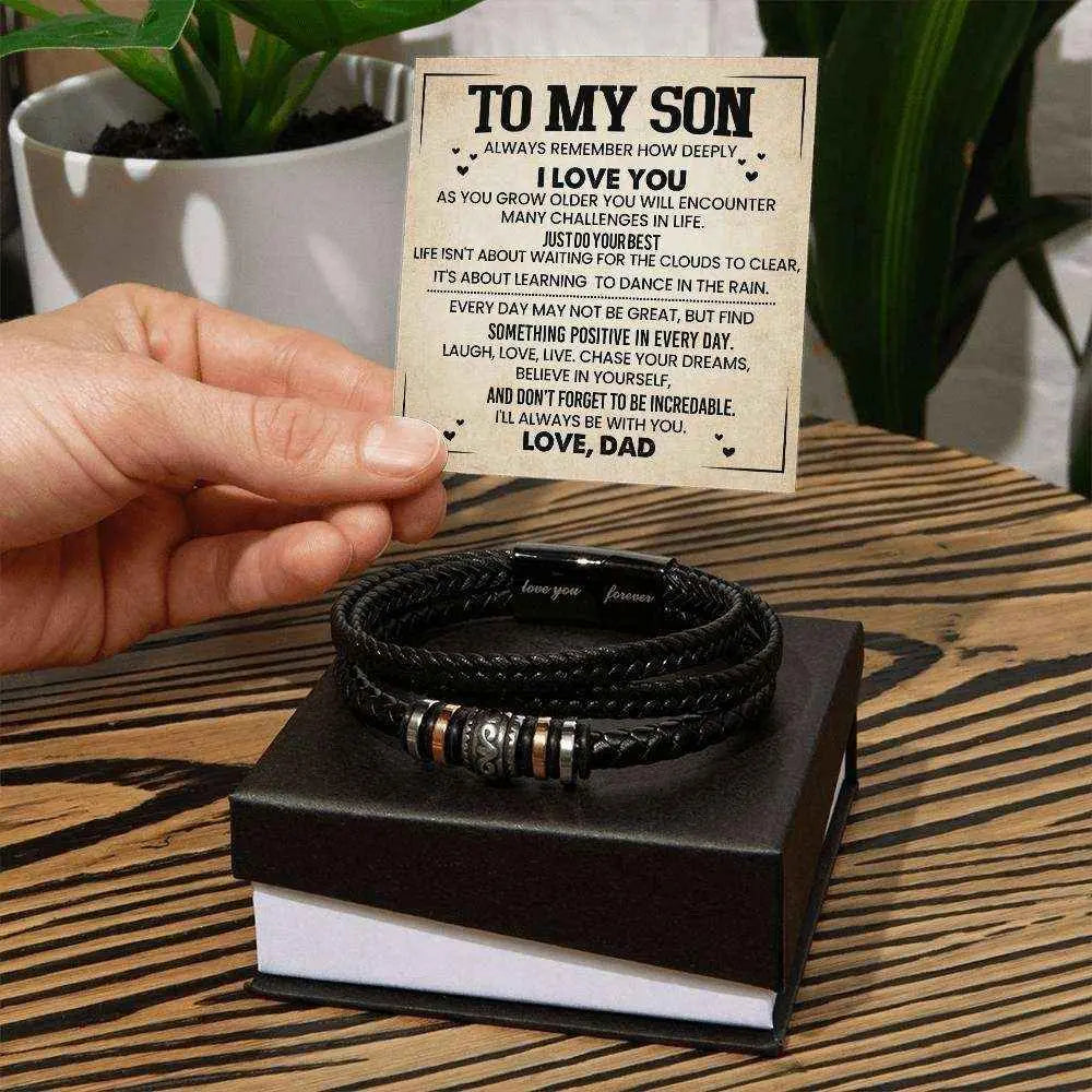 Stack of black braided bracelets on a box with a card above, on a wooden surface.