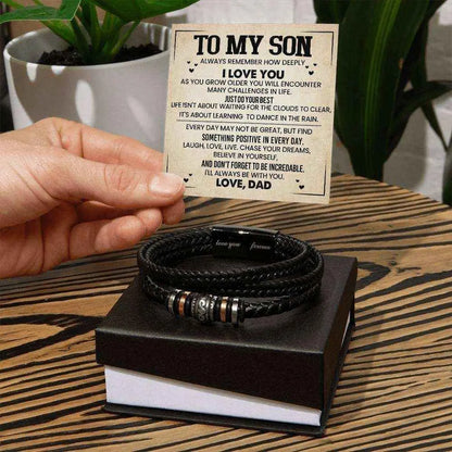 Stack of black braided bracelets on a box with a card above, on a wooden surface.