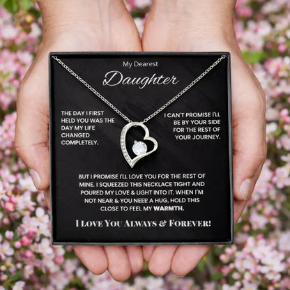 Necklace with heart design held in hands against a blurred floral background