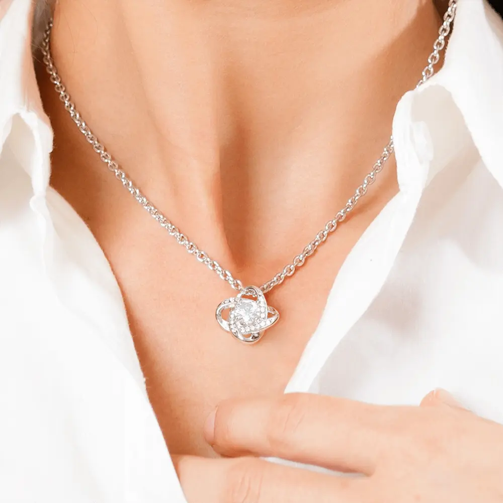 Silver necklace with a heart-shaped pendant worn by a person in a white shirt.