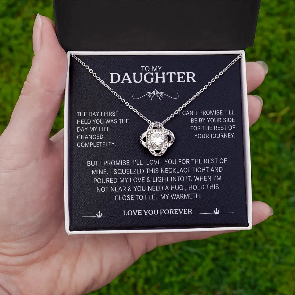 Necklace in a box with a message for a daughter, held by a hand against a grass background.