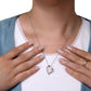 Person wearing a silver heart-shaped necklace with a white background